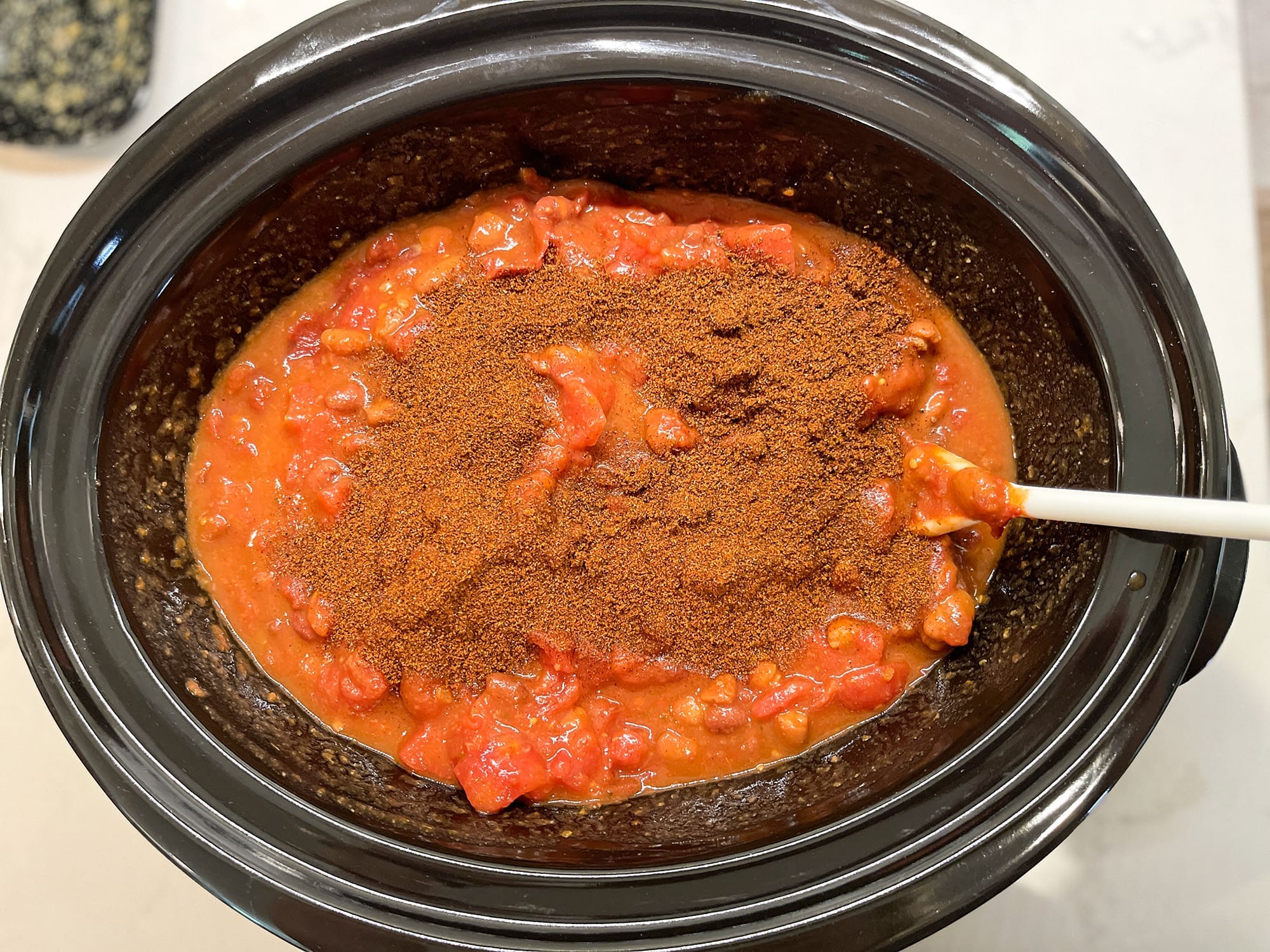 Ingredients in a crockpot with chili seasoning mix on top, ready to be stirred together for an easy crockpot homemade chili recipe.