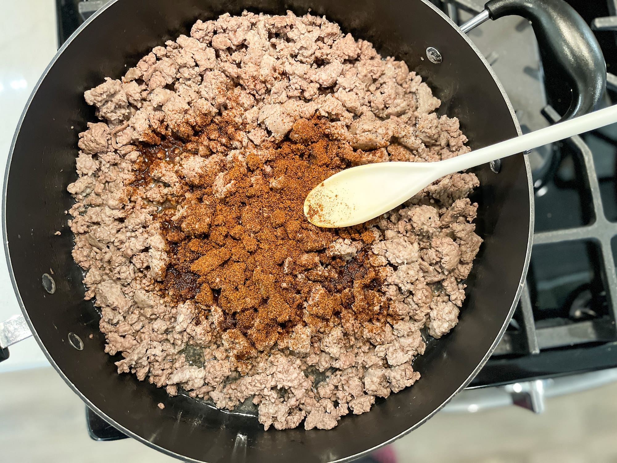 Ground beef and sausage browning in a skillet with seasoning, an essential step in this easy crockpot homemade chili recipe.