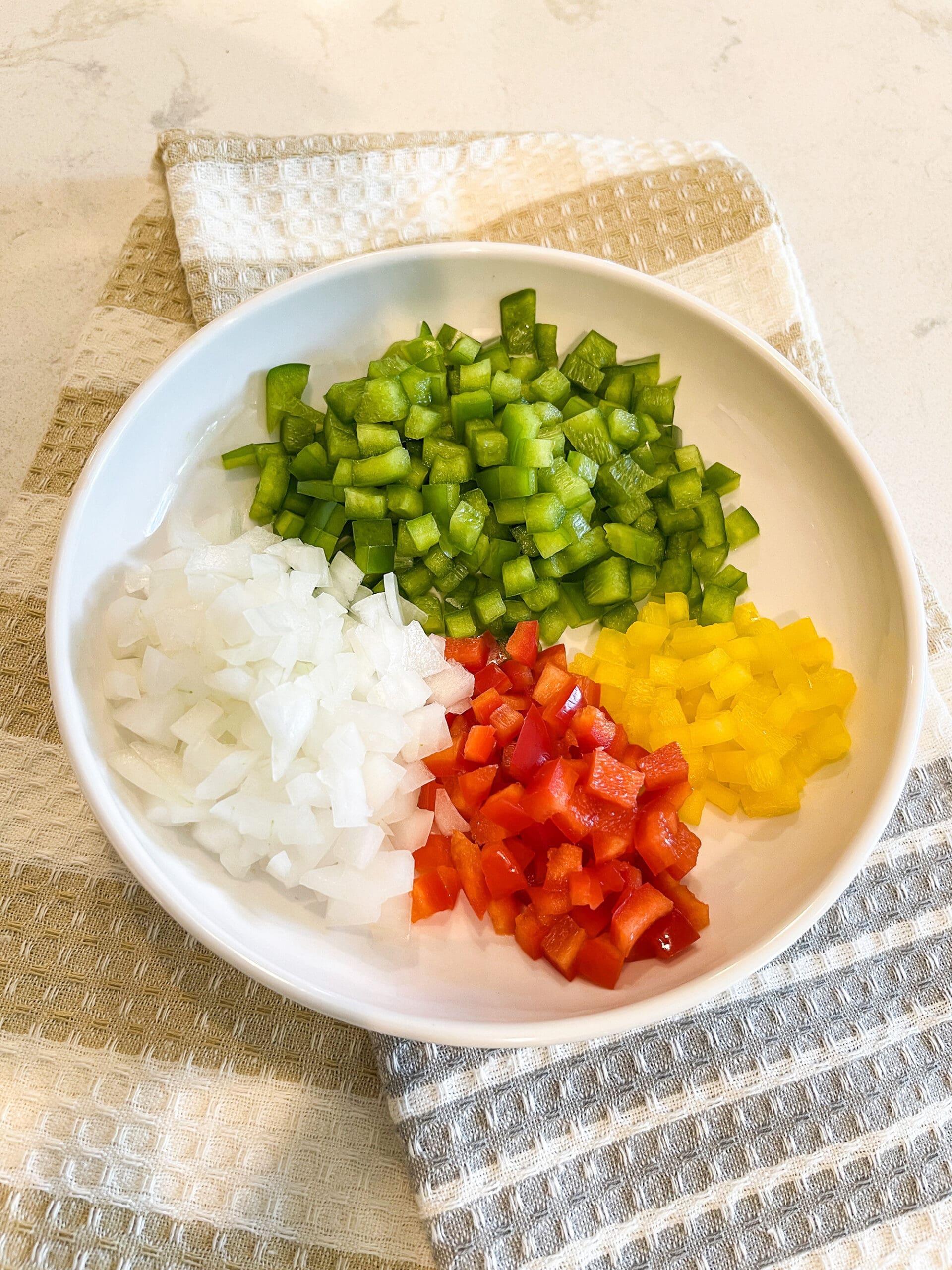 Chopped onions and bell peppers on a white plate, prepped and ready for cooking in an easy crockpot homemade chili recipe.
