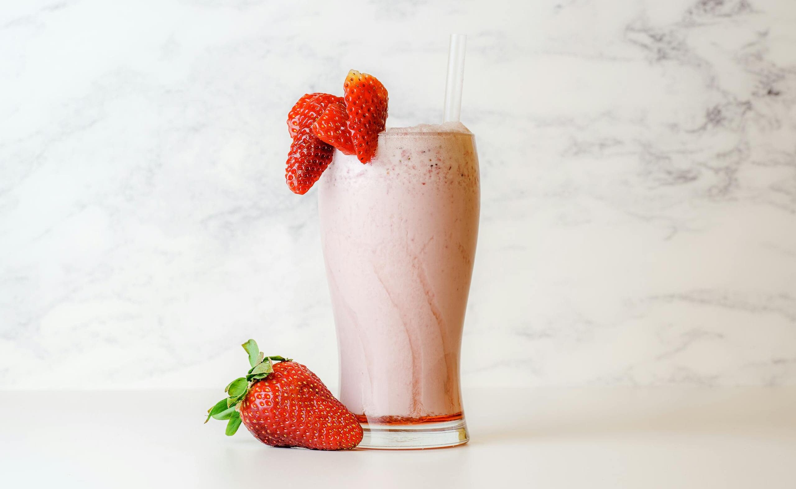 Delicious and creamy strawberry milkshake garnished with fresh berries on a white marble background.